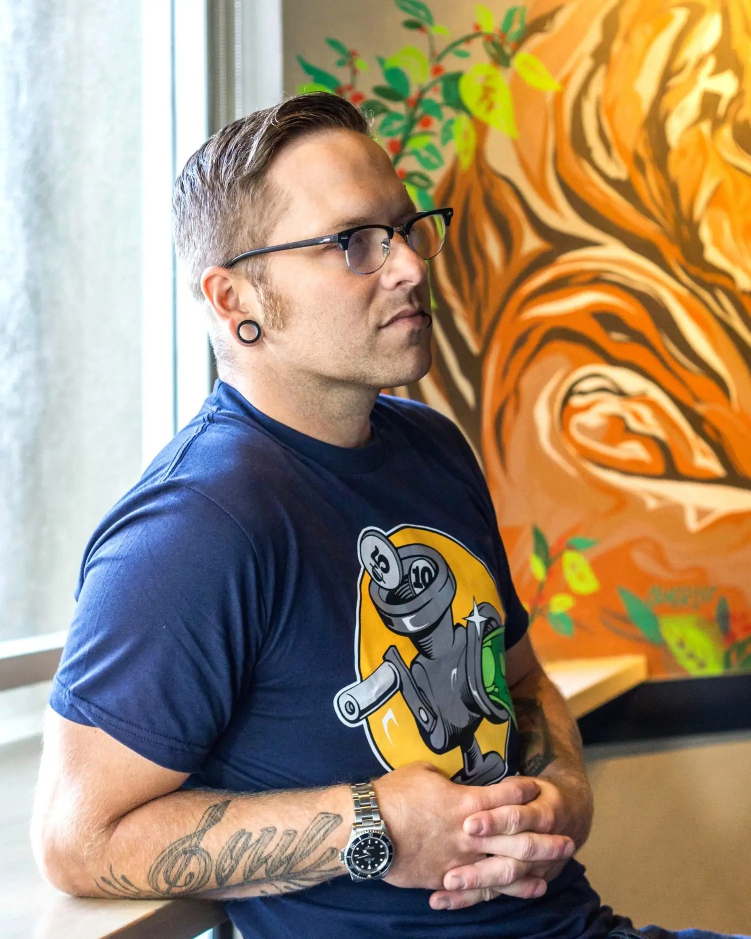 Man with glasses holding a bottle, standing in front of a colorful painting.