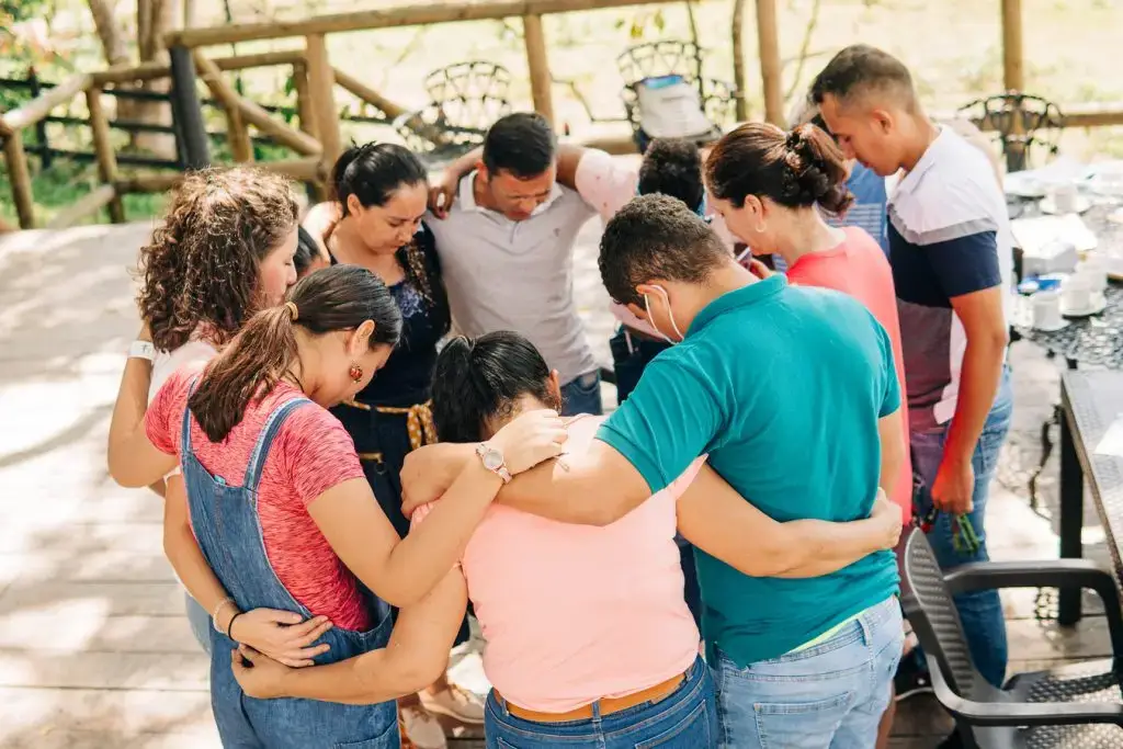 A group of people standing in a circle with heads bowed and arms around each other.