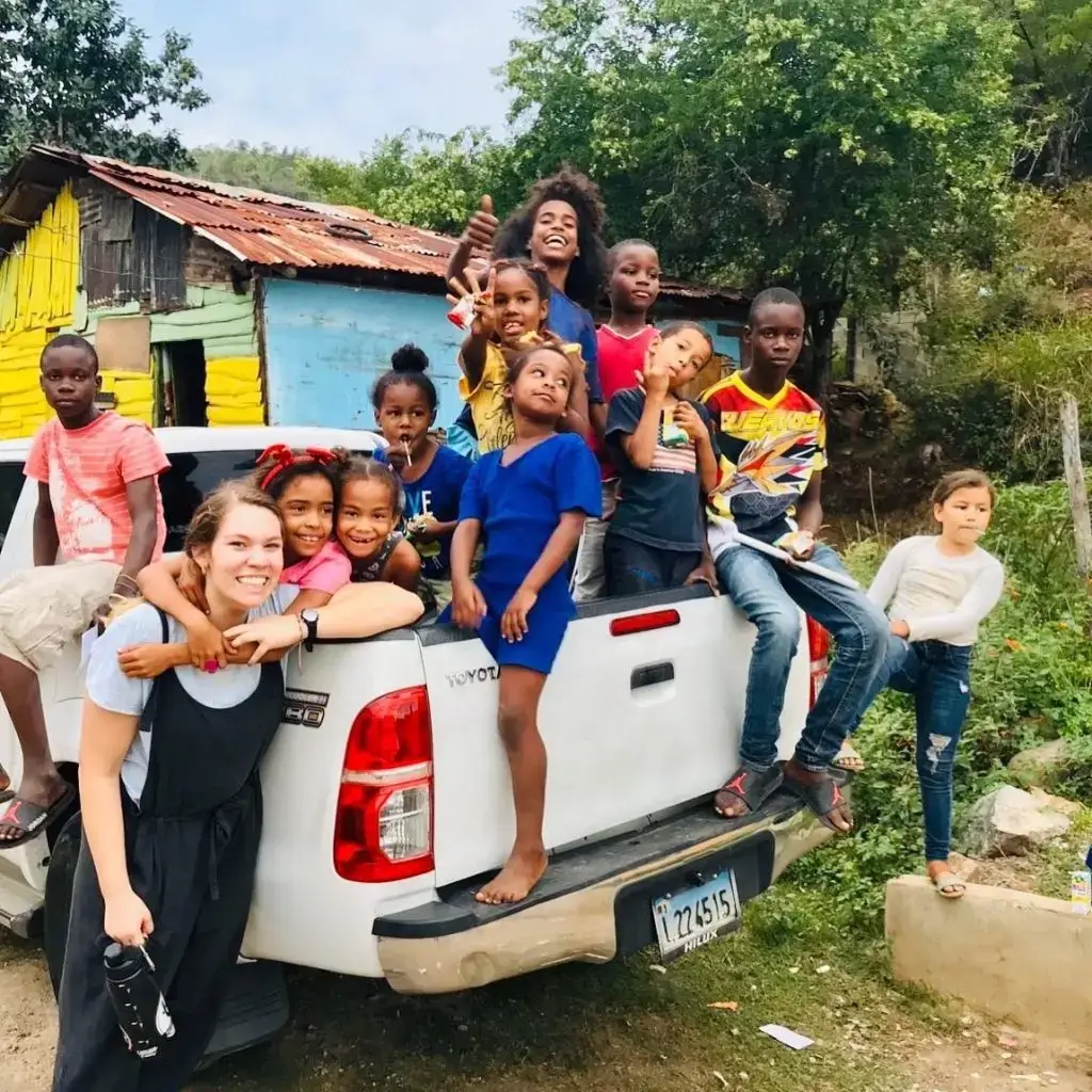 A group of cheerful children and a woman posing around a white pickup truck outdoors.