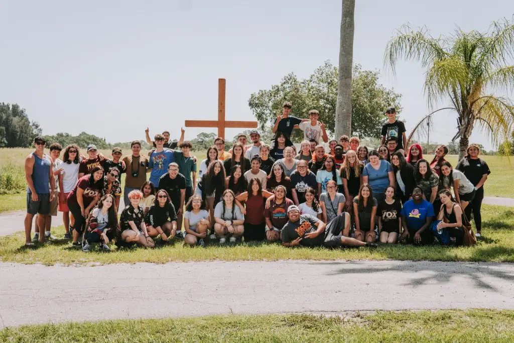 Large group holding flowers and crosses outdoors on a sunny day.