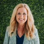 Smiling woman with long blonde hair in a light blazer against a green backdrop.