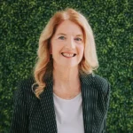 Smiling woman with wavy blonde hair in a pinstripe blazer.