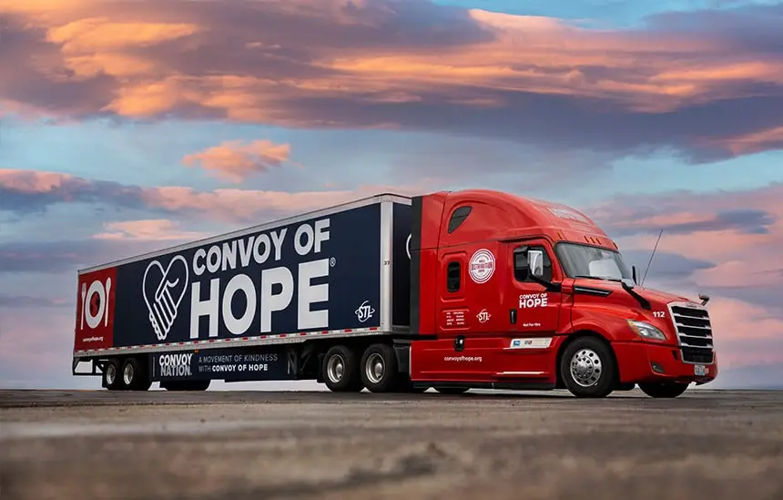 Red truck with Convoy of Hope trailer under a colorful sky.
