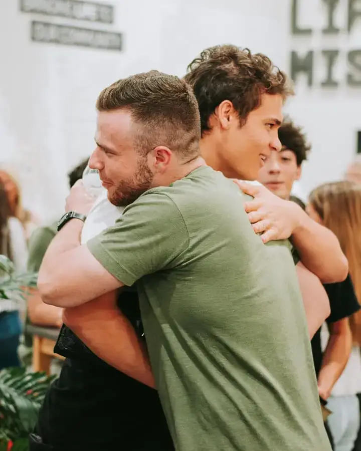 Two men warmly hugging indoors, sharing a joyful moment.