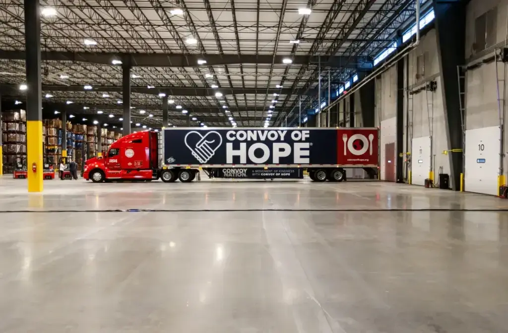 A red truck with a trailer labeled 'Convoy of Hope' inside a warehouse.