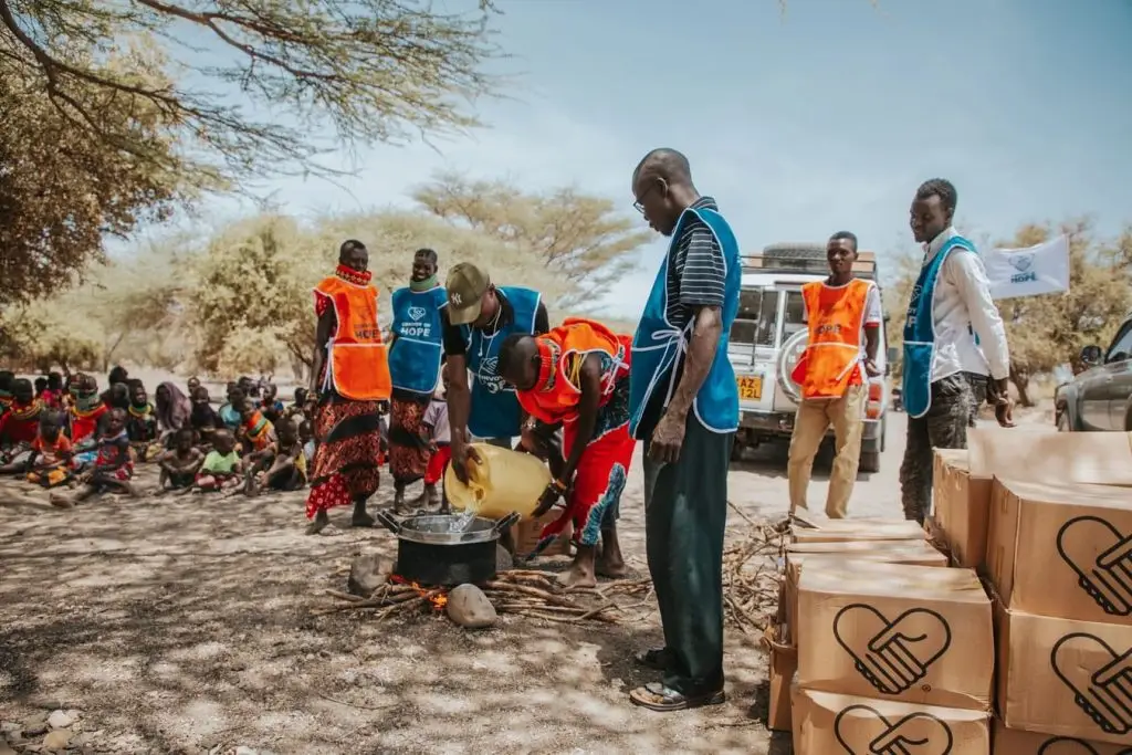 Community members gather outdoors preparing food in large pots.