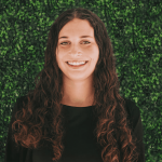 Hailey Bartomeo is smiling, wearing a black shirt, and standing in front of a green background.