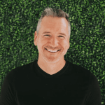 Jonah Sorrentino is smiling, wearing a black shirt, and standing in front of a green background.