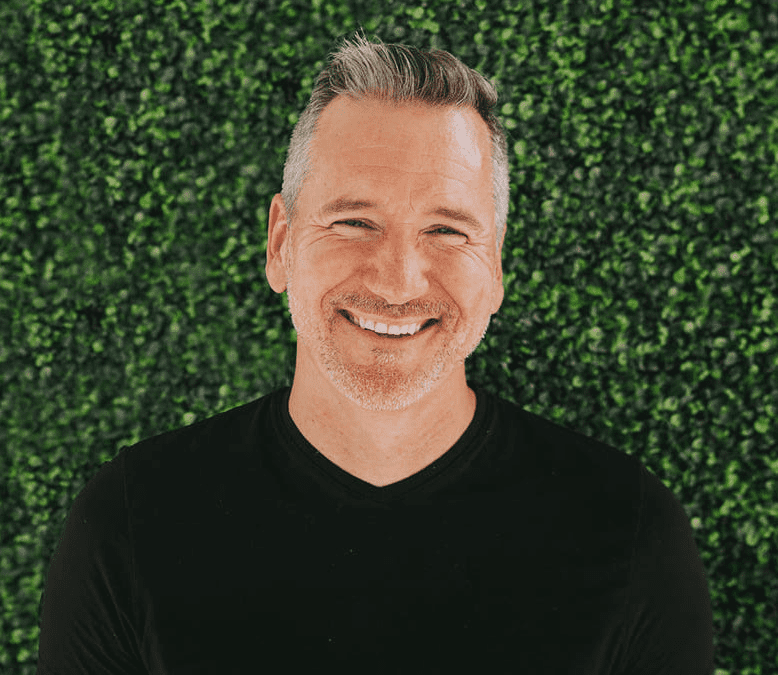 Jonah Sorrentino is smiling, wearing a black shirt, and standing in front of a green background.