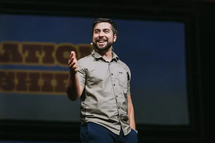 Man smiling and speaking on stage with a microphone headset.