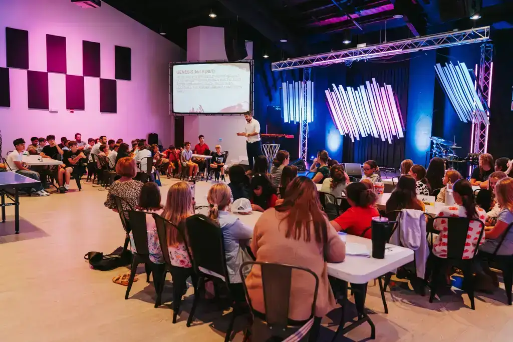 People attending a presentation in a large hall with stage lighting.