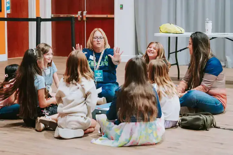 A woman leads a group of children in an interactive activity indoors.