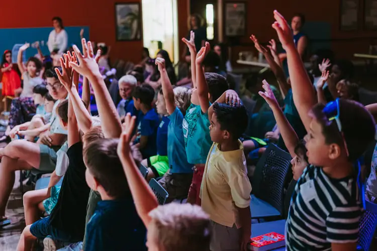 Children raising their hands eagerly in a lively classroom.