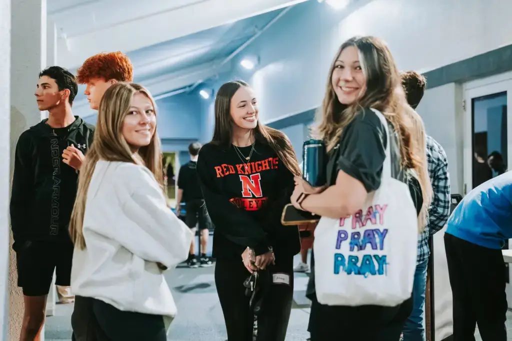 Three young women smiling and standing in a casual indoor setting.