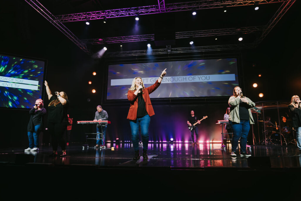 Performers on stage singing with vibrant lighting effects.