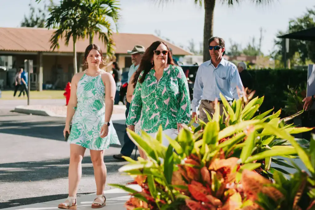 Three people walking outdoors on a sunny day near greenery.