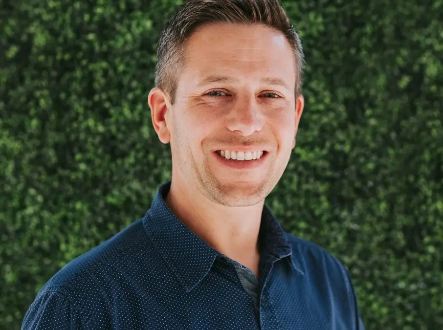 Smiling man in front of green background.