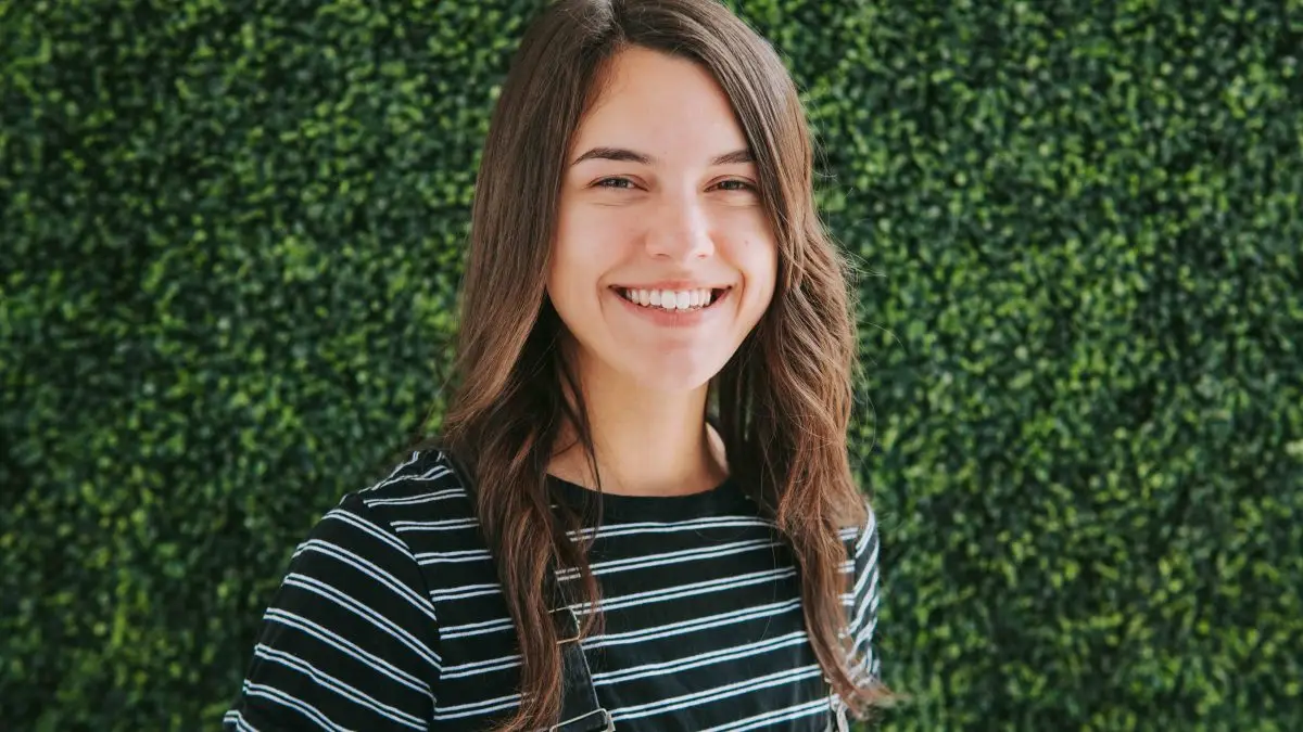 Smiling woman in front of green foliage.