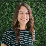Smiling woman in front of green foliage.